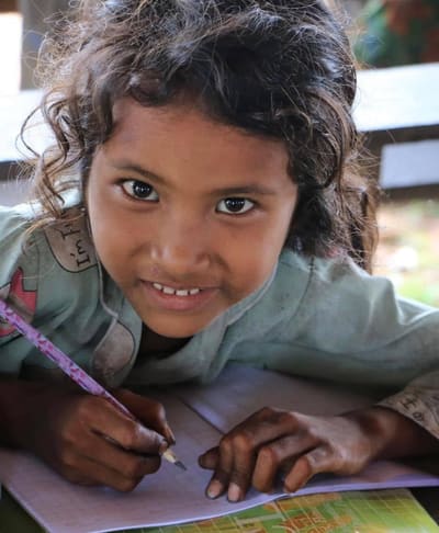 A young indigenous girl smiles as she writes in a notebook with a pencil