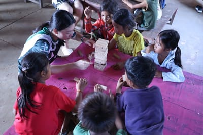 A teacher and children play a wooden block-stacking game together