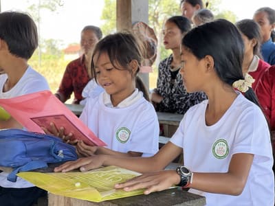 Schoolgirls in REEC t-shirts reading books at an outdoor learning session