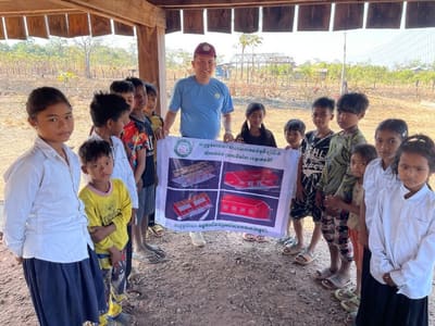 REEC founder Sytha Nan with village children, holding a poster of a planned rural school