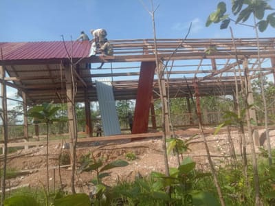 Workers raise the metal roof frame of a new village school on a cleared hilltop