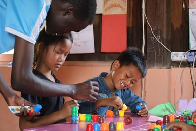 An international student helps two children play with colourful learning toys