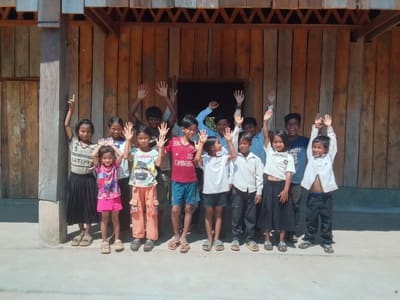 Village children raise their arms and cheer outside their new wooden school