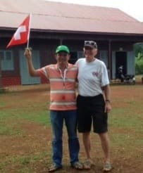 Two men at a REEC-supported school in Ratanakiri, one holding the Swiss flag, marking the EastAid partnership