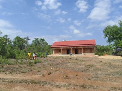 The first REEC-supported school in Lampat — a timber building with a red roof on cleared land