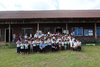About a hundred schoolchildren holding new books gather with teachers and REEC staff in front of their school